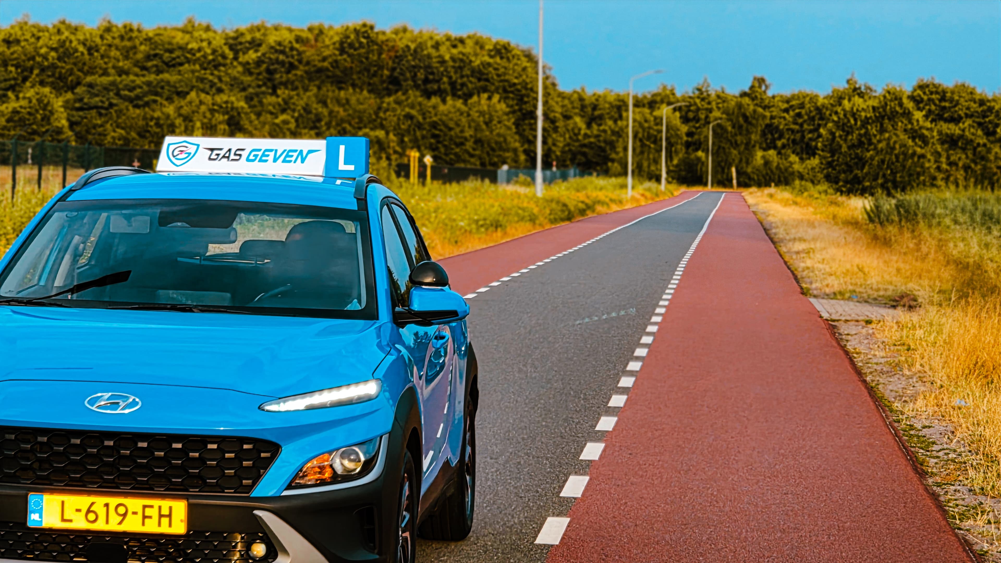 De lesauto van Gas Geven met dakbord op een buitenweg